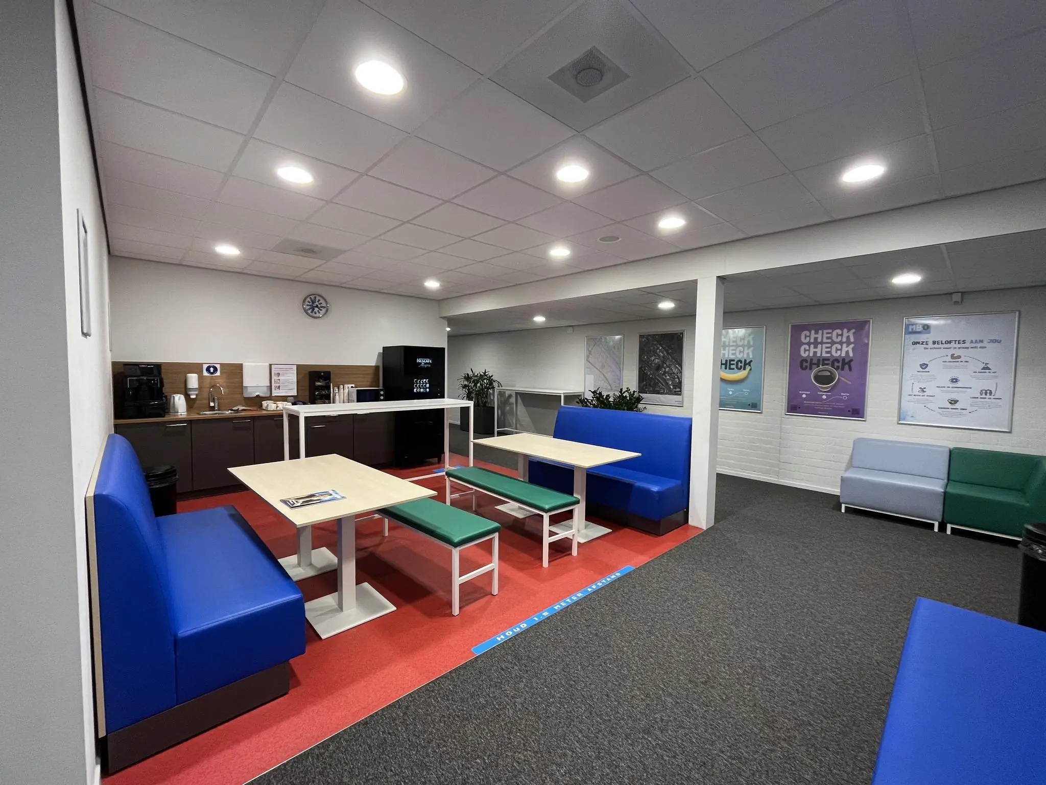 Kantineruimte aan de Niels Bohrweg met zitbanken, tafels, koffiemachines en informatieve posters aan de muur.